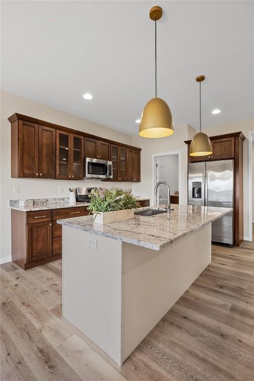 kitchen featuring sink, appliances with stainless steel finishes, a kitchen island with sink, light stone counters, and decorative light fixtures