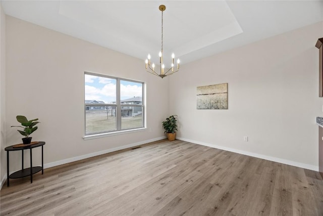 unfurnished dining area with an inviting chandelier, a tray ceiling, and light wood-type flooring