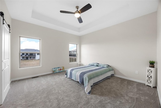 carpeted bedroom with a tray ceiling, a barn door, and ceiling fan