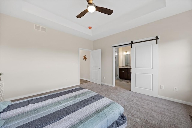 unfurnished bedroom featuring ensuite bathroom, light carpet, a tray ceiling, ceiling fan, and a barn door