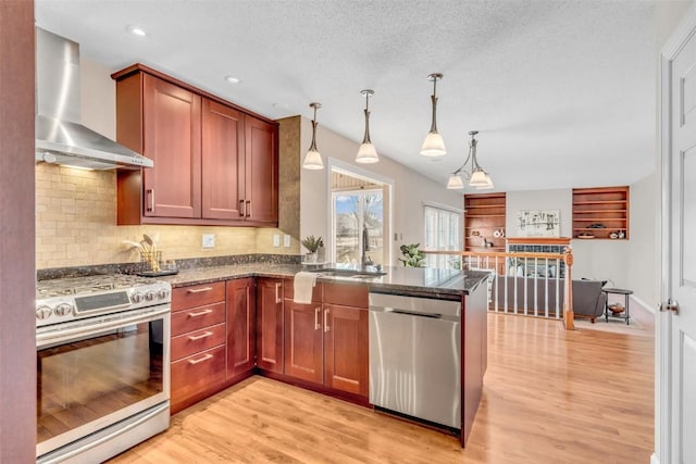 kitchen featuring sink, decorative light fixtures, kitchen peninsula, stainless steel appliances, and wall chimney range hood