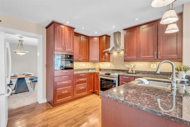 kitchen with pendant lighting, wall chimney exhaust hood, stainless steel range oven, and sink