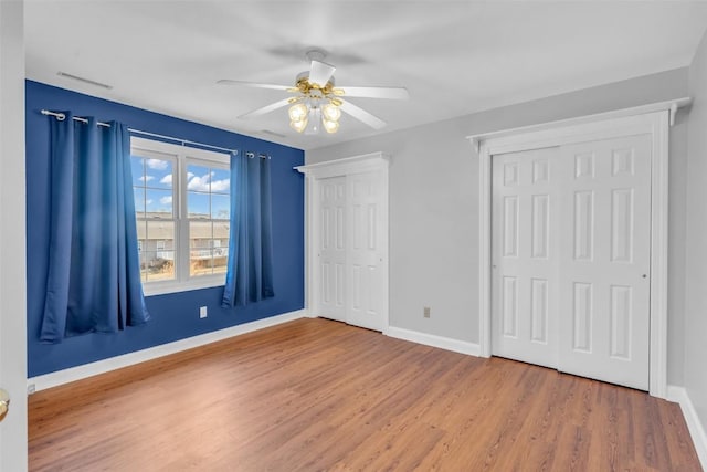 unfurnished bedroom with hardwood / wood-style flooring, ceiling fan, and two closets