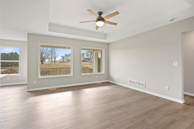 unfurnished room with ceiling fan, a tray ceiling, and light hardwood / wood-style floors