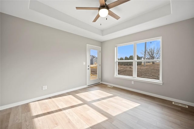 empty room with a tray ceiling, light hardwood / wood-style floors, and ceiling fan