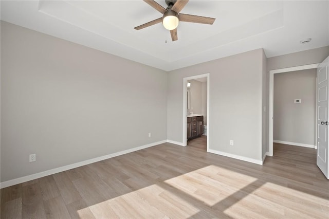 unfurnished bedroom with a tray ceiling, light hardwood / wood-style flooring, ensuite bath, and ceiling fan