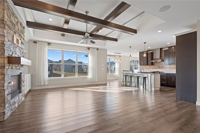 unfurnished living room with beamed ceiling, a fireplace, dark hardwood / wood-style flooring, and ceiling fan with notable chandelier