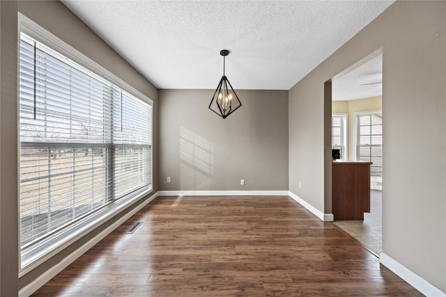 unfurnished dining area with dark hardwood / wood-style flooring, a notable chandelier, and a textured ceiling