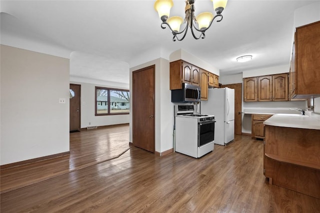 kitchen with sink, white appliances, hanging light fixtures, dark hardwood / wood-style floors, and a notable chandelier