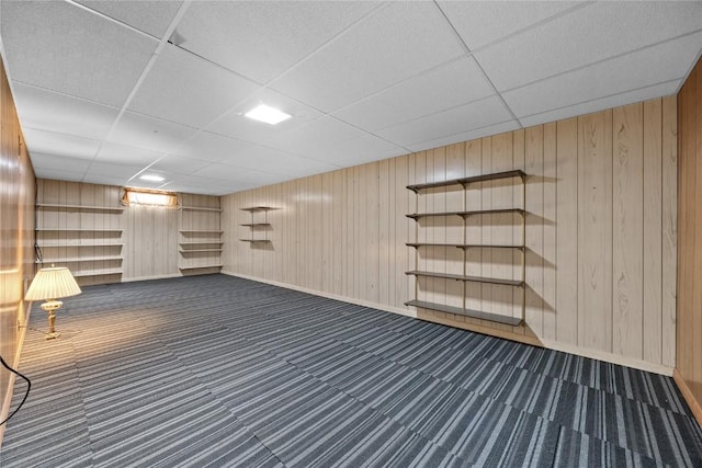 basement featuring a drop ceiling, wood walls, and dark colored carpet