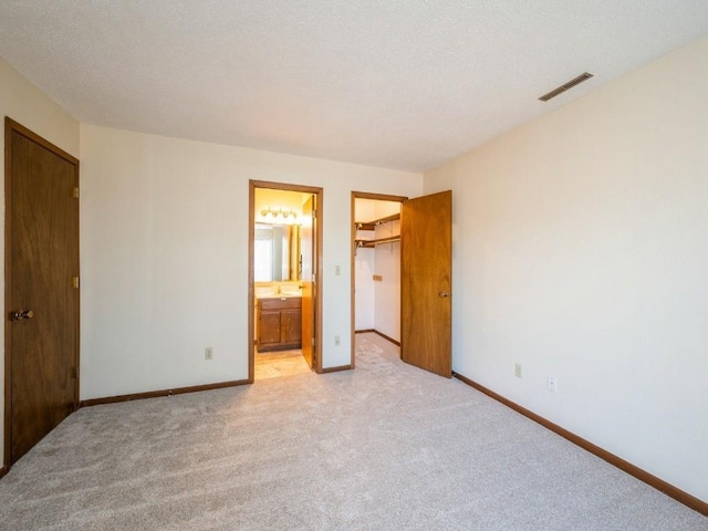 unfurnished bedroom featuring a closet, ensuite bath, light carpet, and a walk in closet