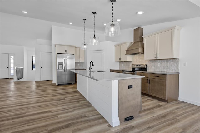 kitchen with premium range hood, sink, decorative light fixtures, stainless steel appliances, and a kitchen island with sink