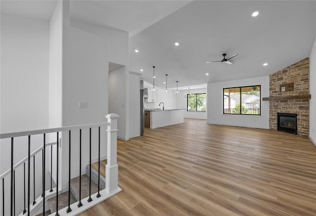 unfurnished living room with lofted ceiling, sink, light hardwood / wood-style flooring, ceiling fan, and a large fireplace