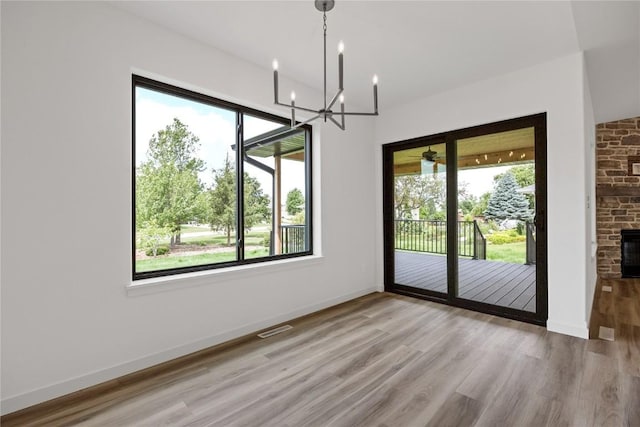 unfurnished dining area with a stone fireplace, a notable chandelier, and light wood-type flooring