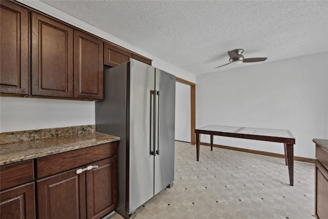 kitchen with ceiling fan, high end fridge, dark brown cabinetry, light stone countertops, and a textured ceiling