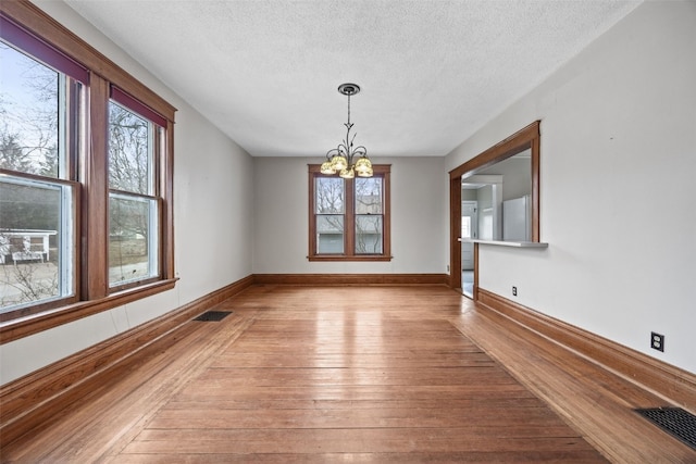 unfurnished dining area featuring a notable chandelier, a wealth of natural light, light hardwood / wood-style flooring, and a textured ceiling