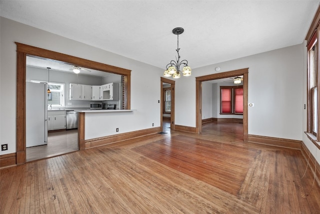 unfurnished living room featuring ceiling fan with notable chandelier and hardwood / wood-style floors