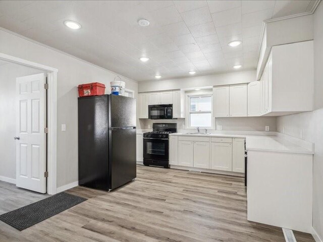 kitchen with sink, black appliances, light hardwood / wood-style flooring, ornamental molding, and white cabinets