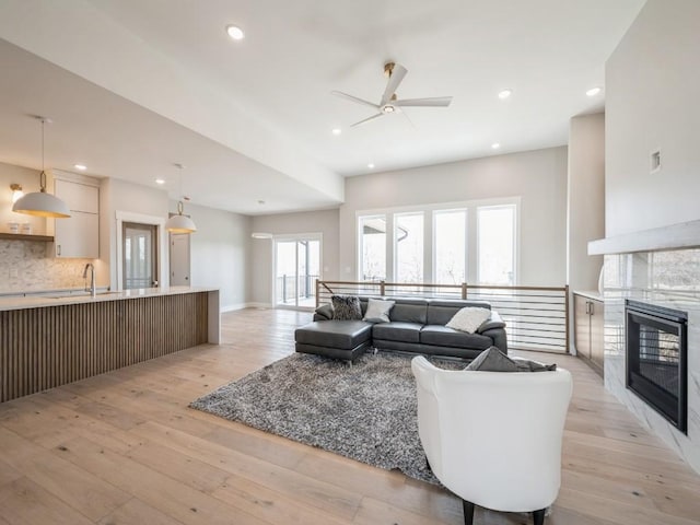 living room with a tile fireplace, sink, ceiling fan, and light hardwood / wood-style floors