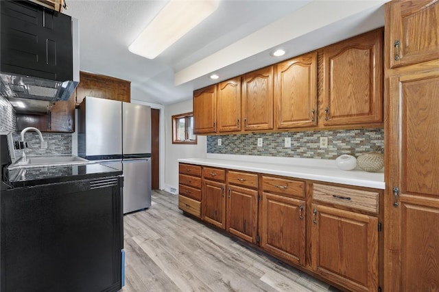 kitchen with stainless steel refrigerator, sink, decorative backsplash, and light wood-type flooring