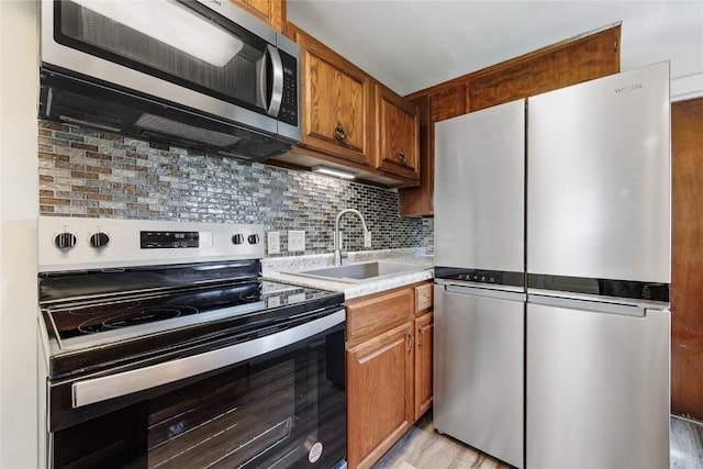 kitchen featuring appliances with stainless steel finishes, sink, light hardwood / wood-style flooring, and decorative backsplash