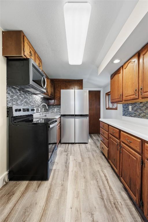 kitchen with stainless steel appliances, sink, light wood-type flooring, and decorative backsplash