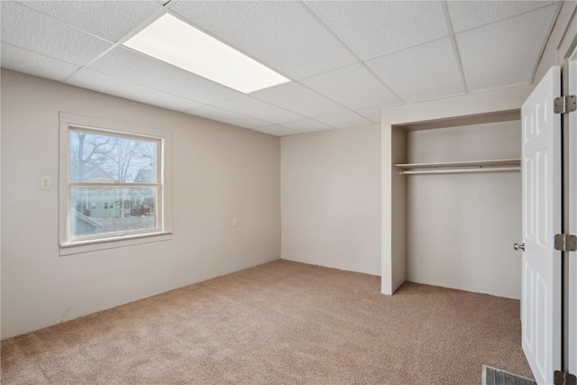 unfurnished bedroom featuring light carpet, a paneled ceiling, and a closet