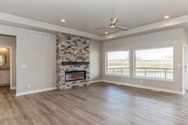 unfurnished living room with ceiling fan, a tray ceiling, a fireplace, and light hardwood / wood-style floors