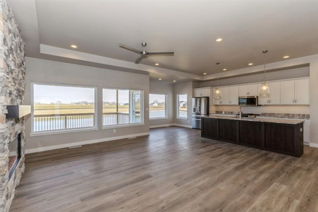 kitchen with white cabinetry, hanging light fixtures, stainless steel appliances, a water view, and a center island with sink