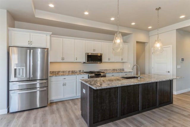 kitchen with appliances with stainless steel finishes, decorative light fixtures, white cabinetry, an island with sink, and sink