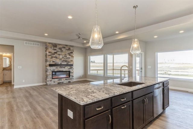 kitchen with sink, hanging light fixtures, a tray ceiling, a fireplace, and a kitchen island with sink