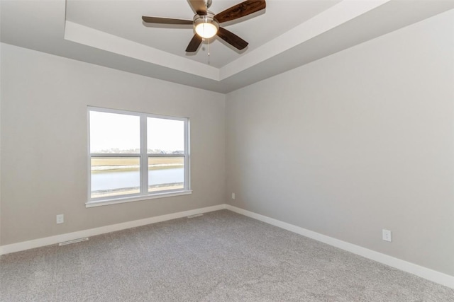 unfurnished room featuring a tray ceiling, a water view, ceiling fan, and carpet flooring