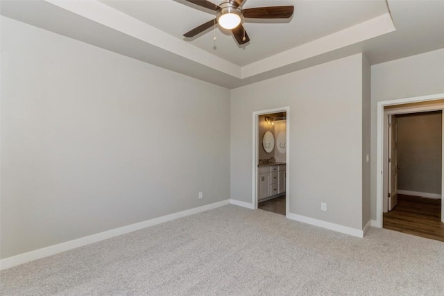 unfurnished bedroom featuring ensuite bathroom, light colored carpet, ceiling fan, and a tray ceiling