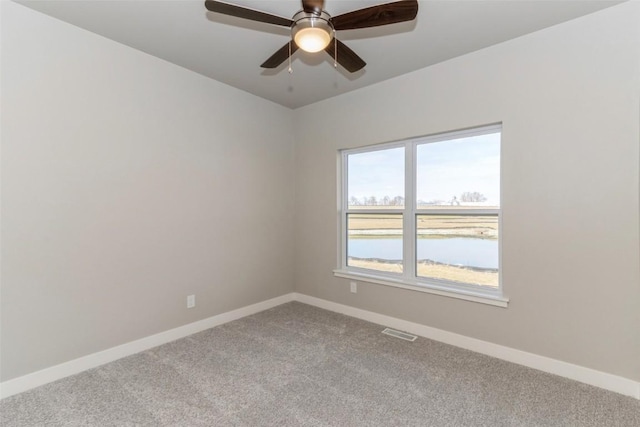 empty room featuring a water view, ceiling fan, and carpet