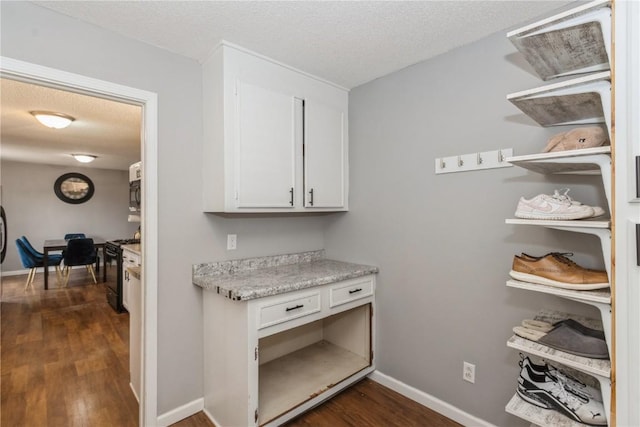 interior space featuring dark wood-type flooring, black range with gas cooktop, a textured ceiling, and white cabinets