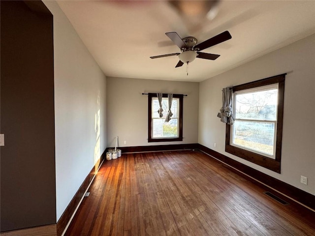 empty room featuring ceiling fan, dark wood-type flooring, and a healthy amount of sunlight