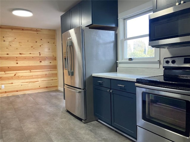 kitchen featuring wooden walls, blue cabinetry, and appliances with stainless steel finishes