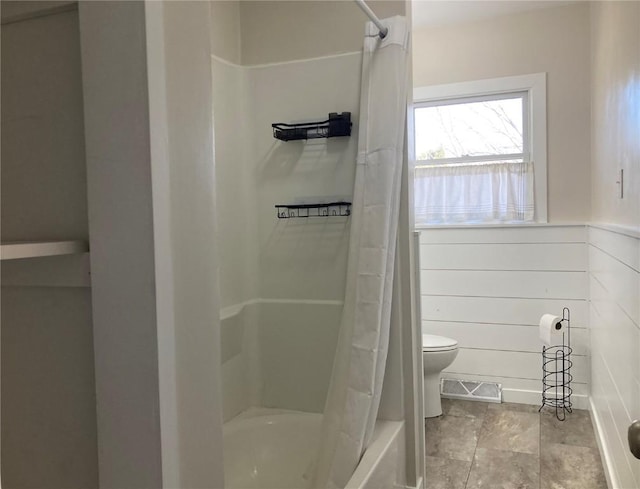 bathroom with shower / tub combo, toilet, and wood walls