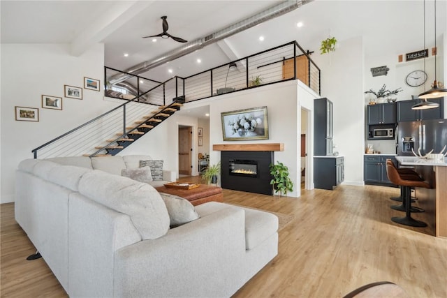 living room with a towering ceiling, beamed ceiling, ceiling fan, and light wood-type flooring