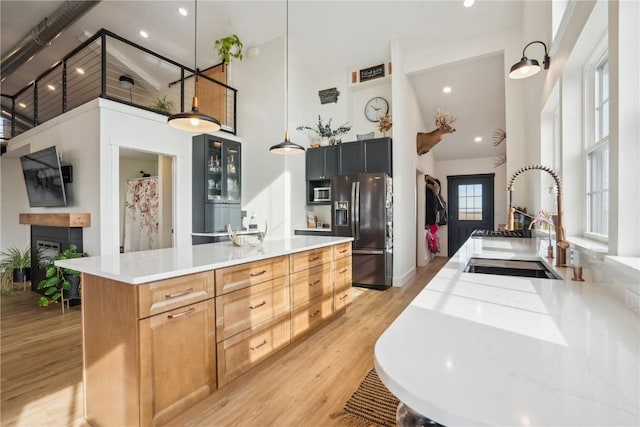 kitchen featuring appliances with stainless steel finishes, pendant lighting, sink, a tiled fireplace, and light wood-type flooring