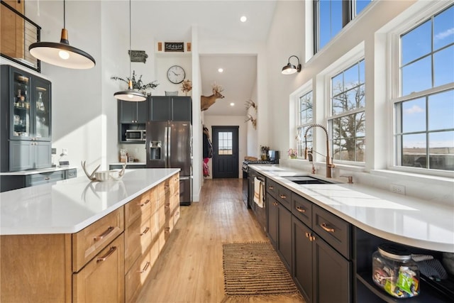 kitchen with pendant lighting, sink, light hardwood / wood-style flooring, stainless steel appliances, and a high ceiling