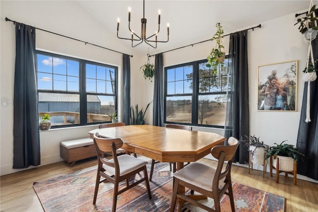 dining space featuring a notable chandelier, wood-type flooring, vaulted ceiling, and a wealth of natural light