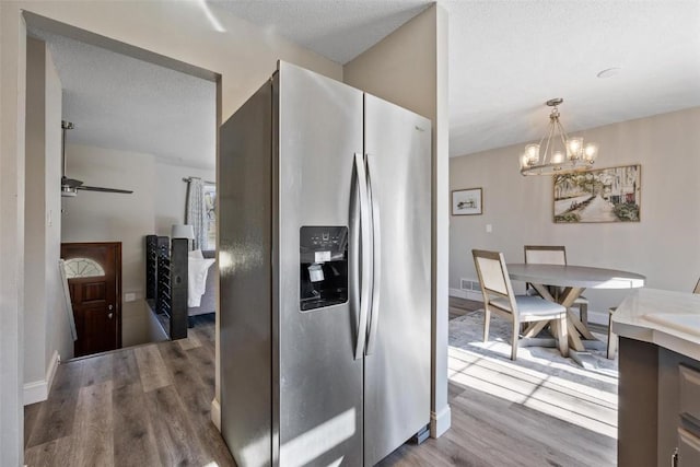 kitchen featuring stainless steel fridge with ice dispenser, hanging light fixtures, a textured ceiling, hardwood / wood-style floors, and ceiling fan with notable chandelier