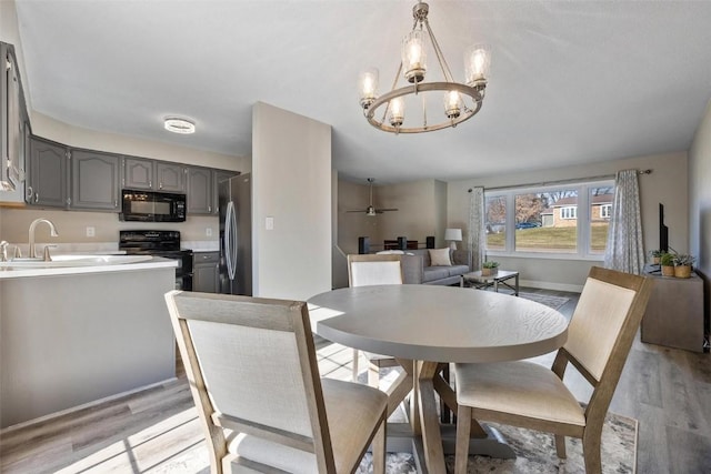 dining area featuring ceiling fan with notable chandelier, sink, and light hardwood / wood-style floors