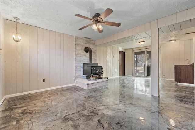 unfurnished living room featuring ceiling fan, a wood stove, wooden walls, and a textured ceiling