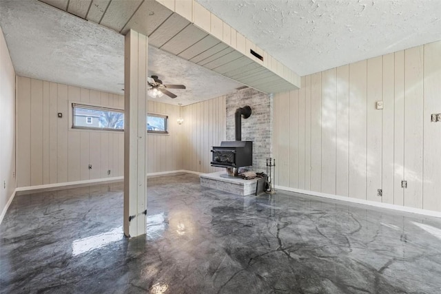 basement with ceiling fan, a textured ceiling, and a wood stove