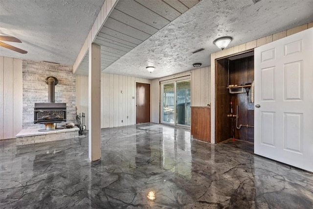 interior space with a wood stove, a textured ceiling, and wood walls