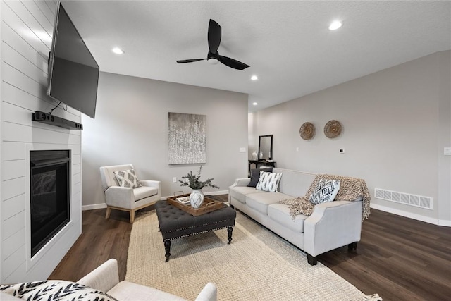 living room featuring dark hardwood / wood-style floors, a large fireplace, and ceiling fan