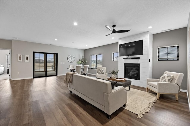 living room with ceiling fan, a large fireplace, dark hardwood / wood-style flooring, and a textured ceiling