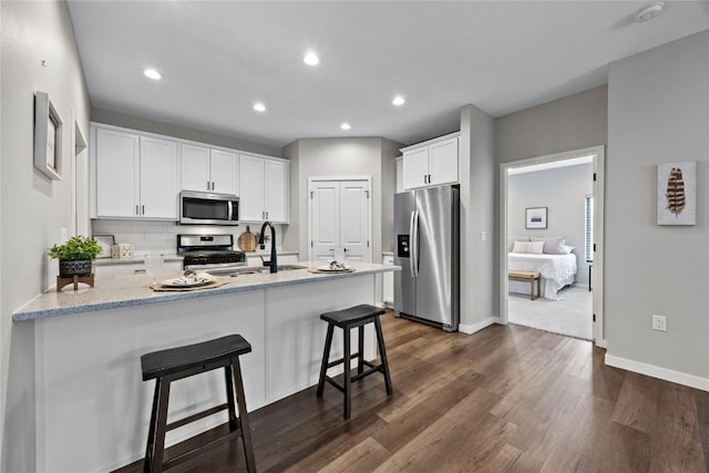 kitchen featuring dark wood-type flooring, stainless steel appliances, light stone countertops, white cabinets, and a kitchen bar